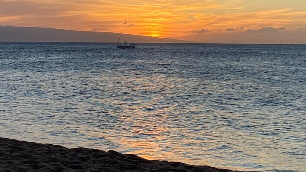 Ein Strand mit einem Segelboot auf ruhigem Wasser bei Sonnenuntergang.