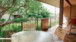 Ein Balkon mit einem Glastisch und zwei Stühlen, der einen üppigen Garten und ein Gebäude im Hintergrund zeigt.
