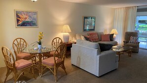 Ein Wohnzimmer mit Esstisch aus Glas, Korbstühlen, einem grauen Sofa, einem Couchtisch und einem Deckenventilator.