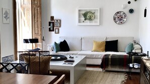 Un salon comprenant un canapé, une table basse et une table à manger. Une porte donne accès à une autre pièce, et un mur est décoré de tableaux encadrés.