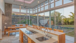 A modern kitchen with large windows, a dining area, and a view of a swimming pool and garden. - Spacious Modern Home w/pool in gated community (Playa Guiones)