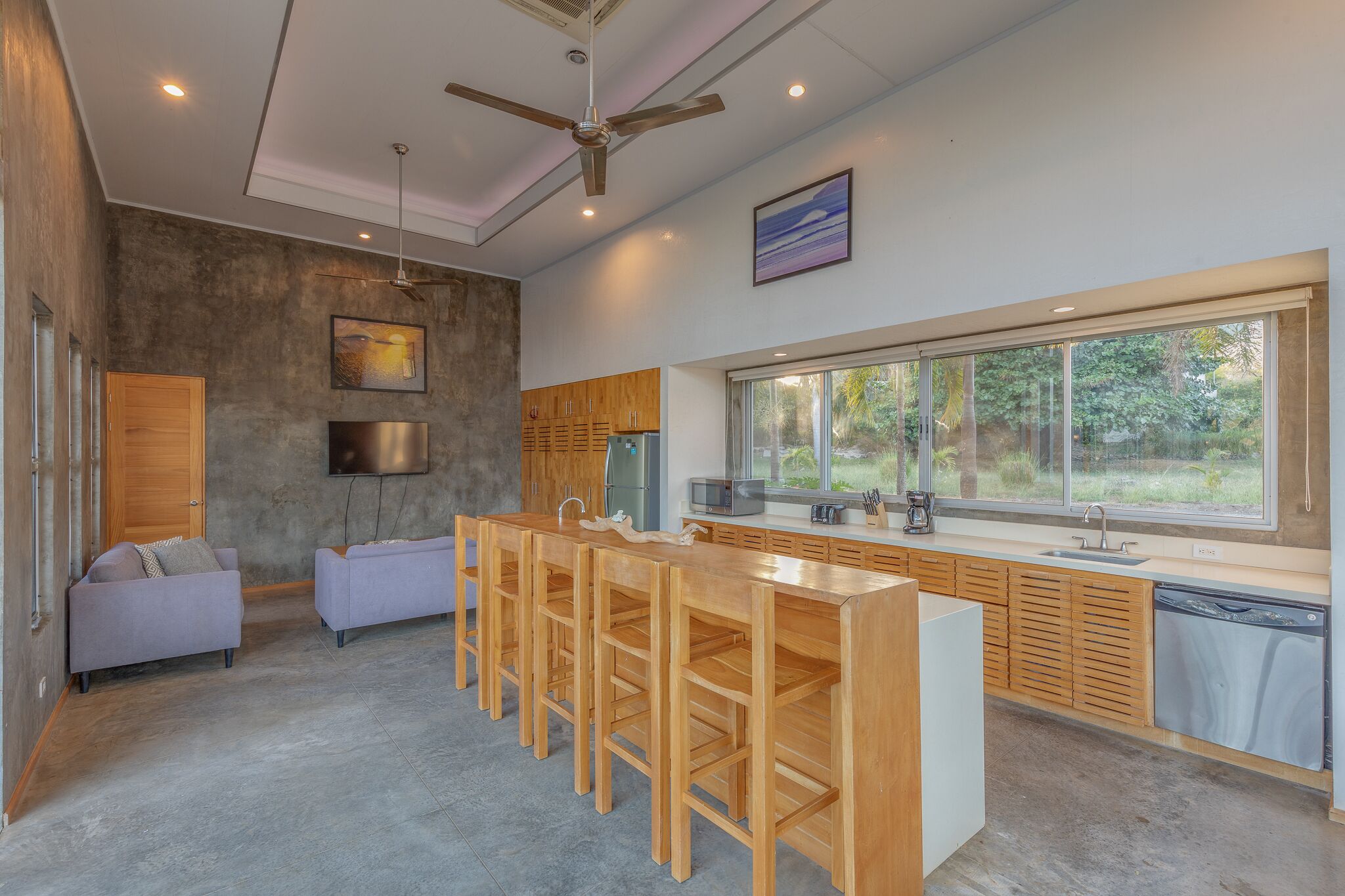 A modern kitchen with a large island, wooden cabinets, and a view of the outdoors.