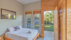 A bedroom with a wooden bed, a large window, and a view of a garden. - Spacious Modern Home w/pool in gated community (Playa Guiones)
