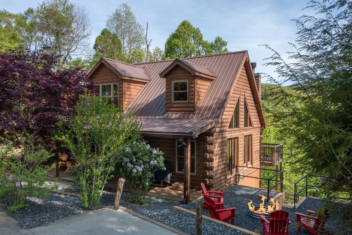 A log cabin with a porch, a fire pit, and red Adirondack chairs.