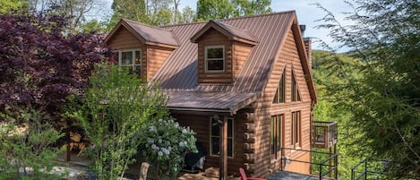A log cabin with a porch, a fire pit, and red Adirondack chairs.