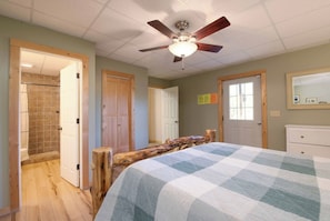 A bedroom with a bed, wooden headboard, ceiling fan, and a view of a bathroom with a shower and toilet. - Heavenly Views~Hot Tub+Fire Pit+Fireplace & WiFi! (Spruce Pine)