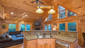 A cabin interior with a kitchen, a dining area, and a living room with a sofa. - Heavenly Mtn Views, Hot Tub+Fire Pit+Grill, Fireplace, WiFi, Hike, Close to BRP! (Spruce Pine)