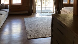 Ein Zimmer mit Holzboden, einer Couch, einem Bett, einem großen Fenster und einer Schiebetür zu einem Außenbereich.