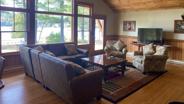 A spacious living room with a high ceiling, large windows, a fireplace, and a television.