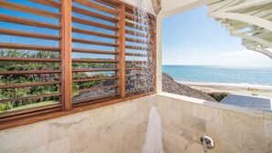 Ein Badezimmer mit Dusche, Meerblick und einem Fenster mit Holzjalousien.