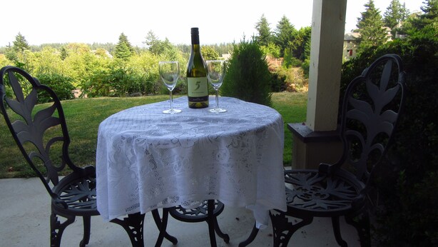 Een ronde tafel met een witte tafellaken van kant, twee wijnglazen en een fles wijn erop.