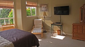 Een slaapkamer met een bed, een stoel, een bureau, een televisie en een dressoir.