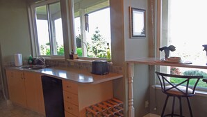 Een keuken met een groot eiland, een wijnrek en een barkruk bij het raam.