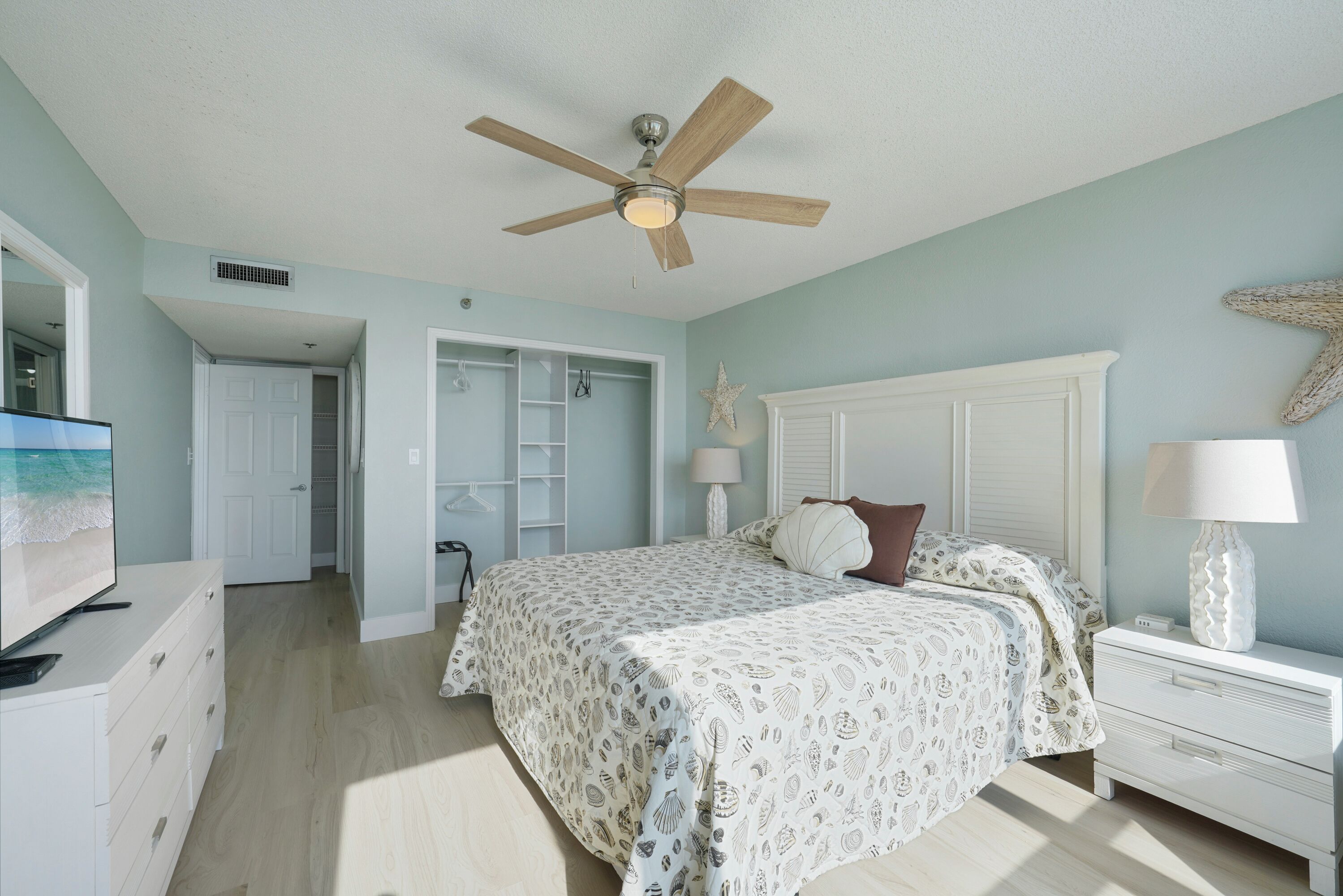 A bedroom with a bed, a ceiling fan, a nightstand, a lamp, and a starfish decoration on the wall.
