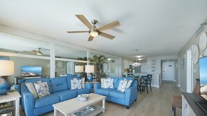 A spacious living room with blue sofas, a coffee table, and a ceiling fan. - JUST RENOVATED! Amazing Views!!! Beautiful Updated 2 Bedroom, 2 Bath condo! (Miramar Beach)