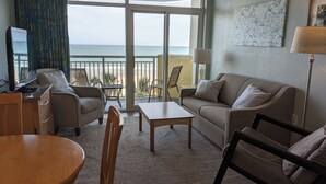 Et hotelværelse med balkon, sofa, sofabord, fjernsyn og skrivebord.