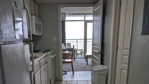 Et smalt køkken med hvide skabe, en mikroovn og et flisegulv, der fører ud til en balkon.