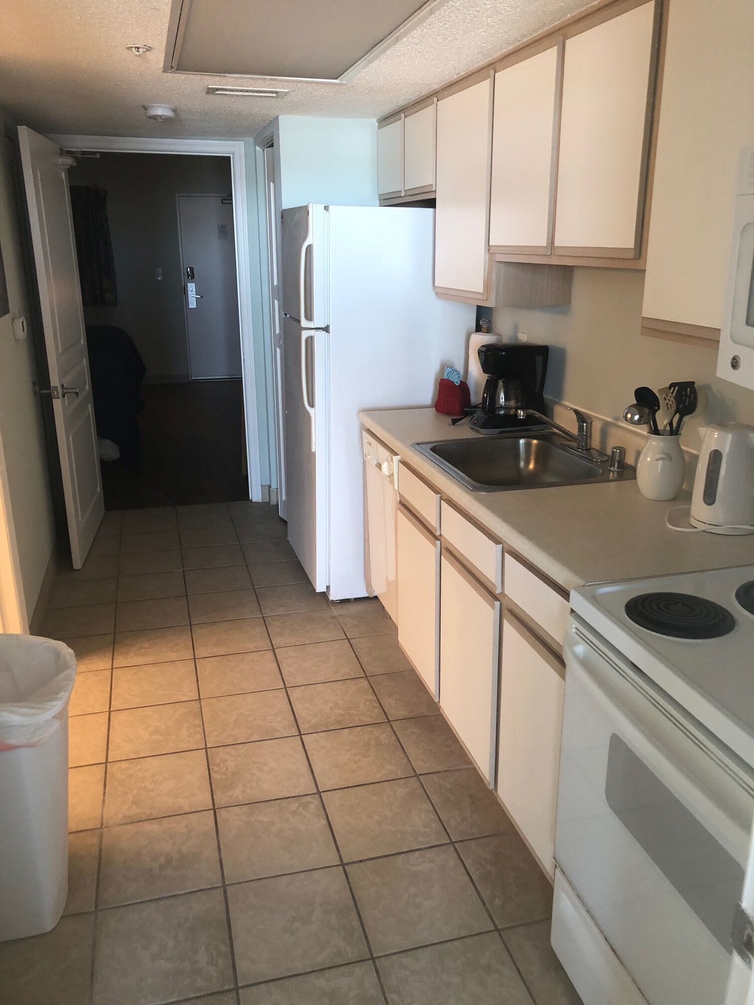 Una cocina compacta con armarios blancos, un refrigerador blanco, una estufa y un lavamanos.