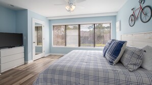Un dormitorio con una cama, un televisor, un ventilador de techo, una ventana con persianas y una bicicleta colgada en la pared.