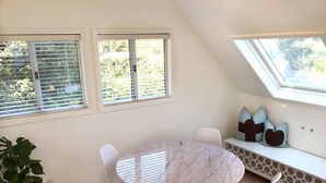A dining area with a round marble table, white chairs, a potted plant, and a bench with cushions. - DETACHED GUEST HOUSE: Walk To Town, 1030 Sq Ft, 1 BR/1.5 BA, Mt. Tam Vie (Mill Valley)