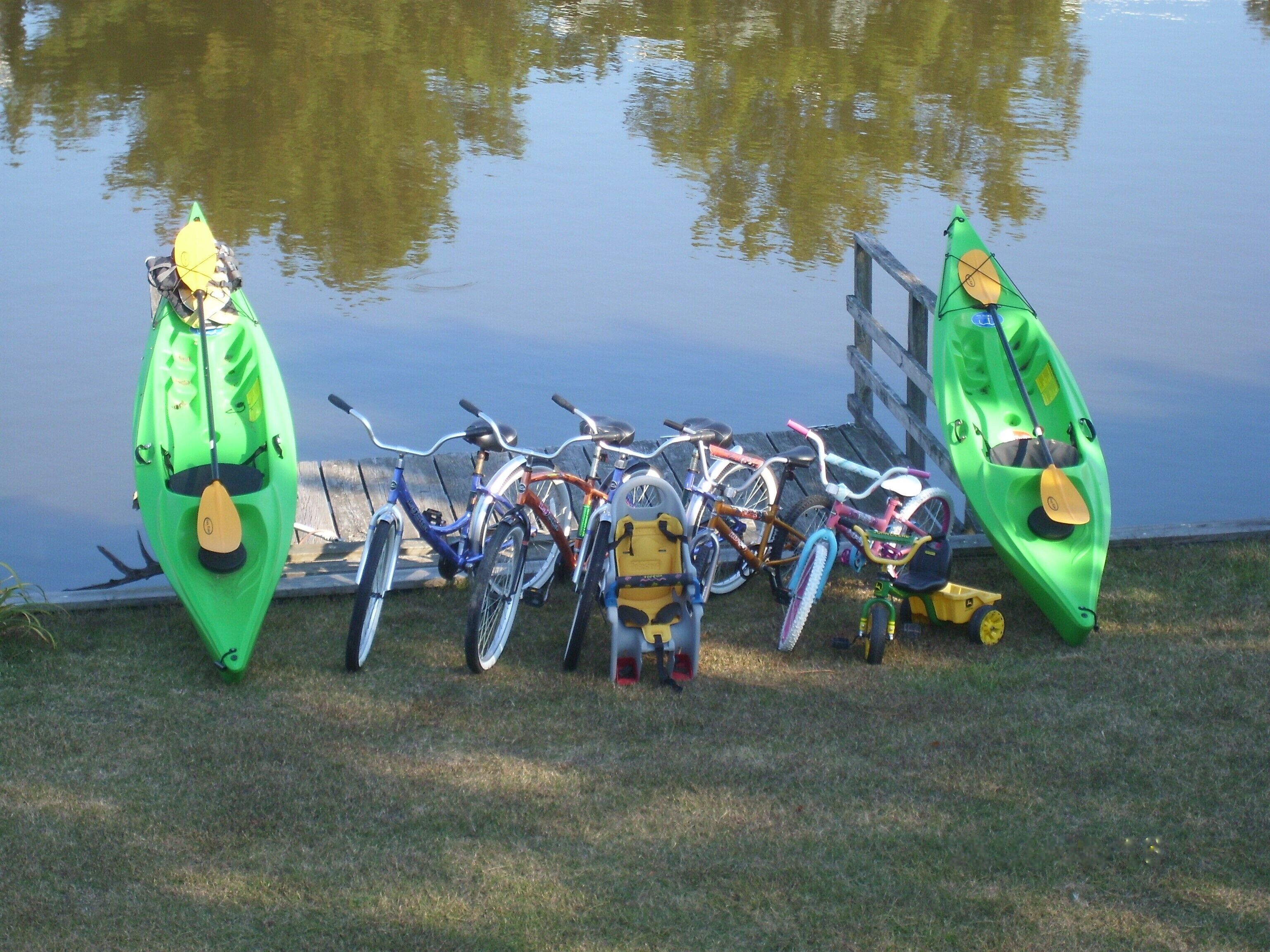 Una hilera de kayaks y bicicletas estacionadas junto a un lago tranquilo.