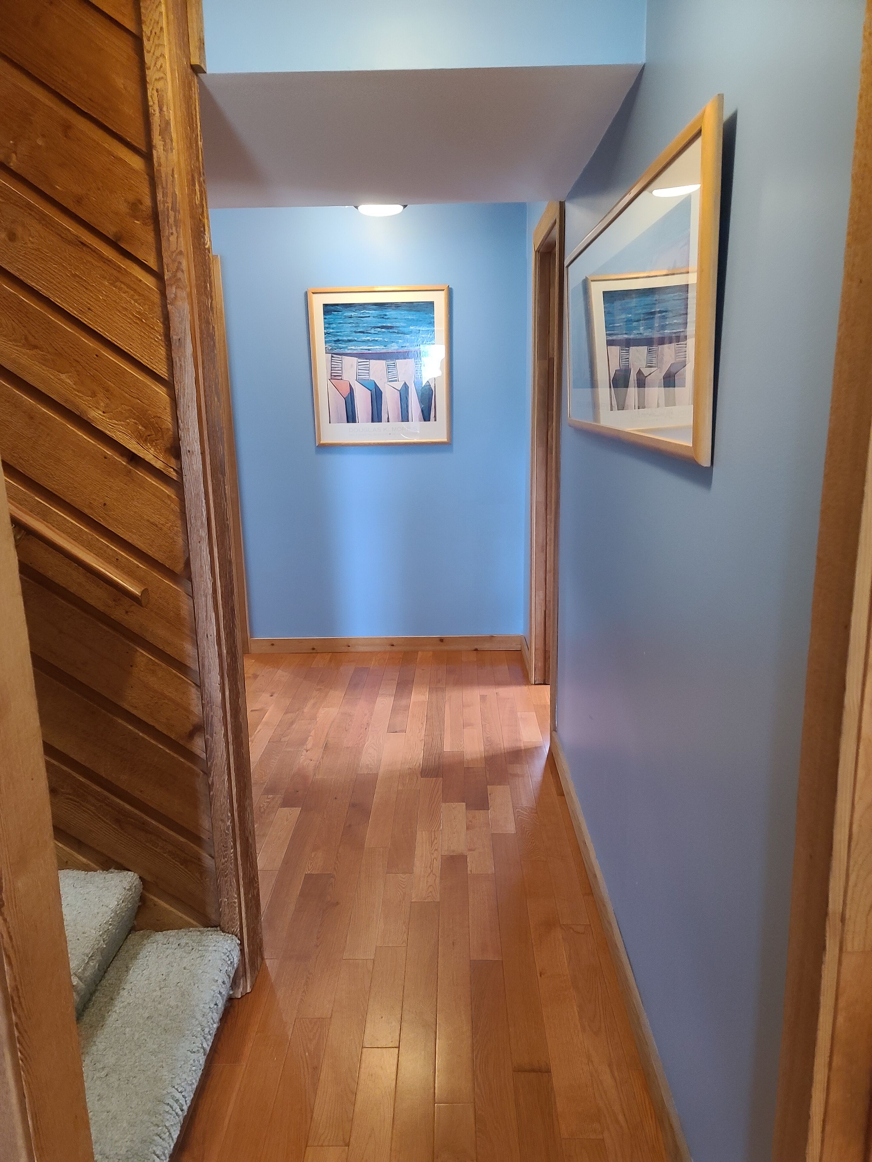 A hallway with wooden flooring, blue walls, and framed artwork.
