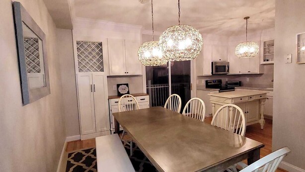 Un comedor con una mesa larga y sillas, una cocina con armarios blancos y lámparas colgantes.