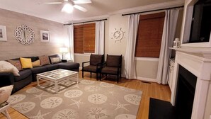 Una sala de estar con sofá, sillas, una mesa de centro, chimenea y un tapete estampado.