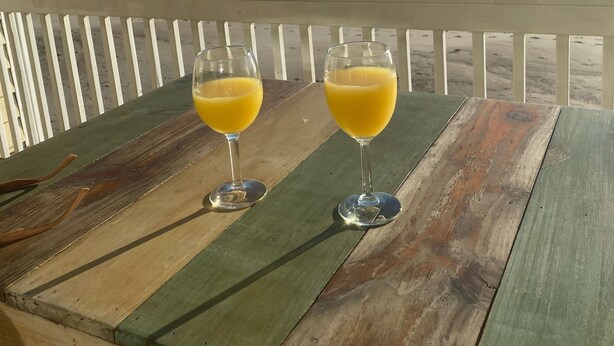 Two glasses of orange juice on a wooden table with a view of the ocean. - Perfect in every Way: Nothing to do but relax (Kure Beach)