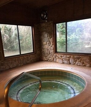 Un jacuzzi en una habitación de paredes de piedra con ventanas amplias.