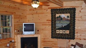 Een knus interieur van een blokhut met een open haard, houten wanden, een televisie en een lijst met een landschapsfoto.