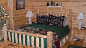 Een slaapkamer in een houten hutje met een bed, twee bedlampjes, een nachtkastje en een klein plankje met decoratieve objecten.