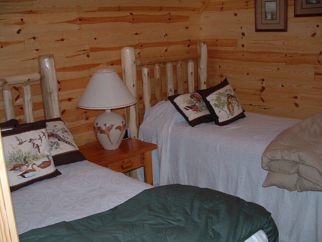 Habitación de cabaña de madera con dos camas, una mesita de noche con lámpara y almohadas decorativas.