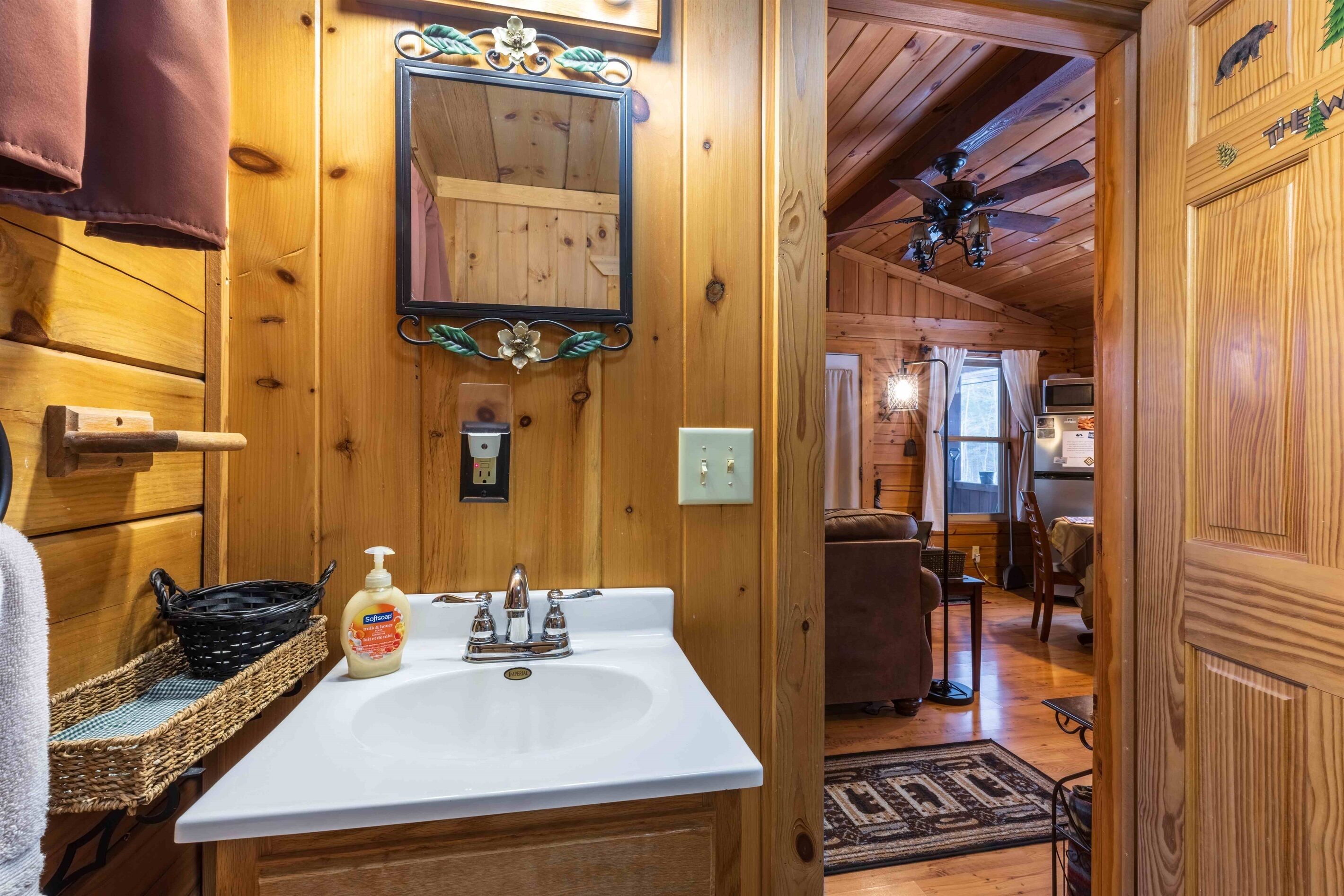 Interior de una cabaña de madera con un lavabo blanco, un espejo y un ventilador de techo.
