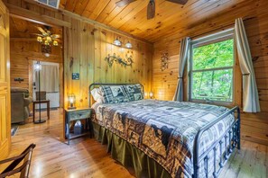 Une chambre à coucher dans une cabane en bois, avec un lit, des tables de chevet, un bureau et une fenêtre donnant sur la forêt.