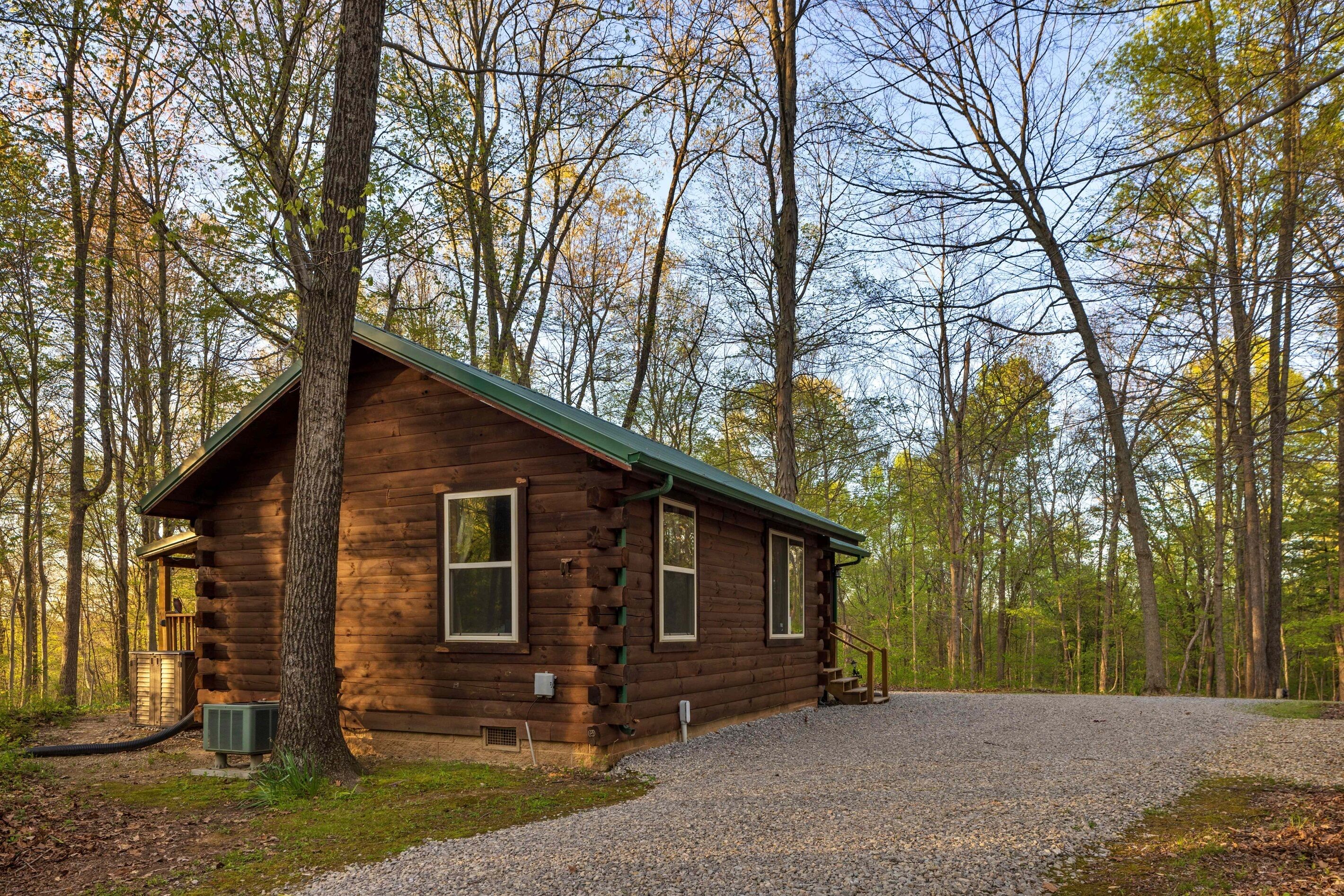 Ein rustikales Holzhaus mit Schotterauffahrt und einer Holzdiele, umgeben von hohen Bäumen.