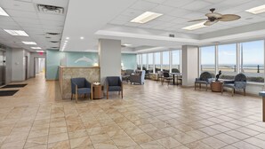 A spacious lobby with a reception desk, seating area, and large windows offering a view of the ocean. - Oceanfront Condo in High Rise in the Heart of the Resort Area (Virginia Beach)