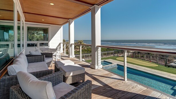 Un espacio exterior techado con mobiliario de mimbre, piscina y vista al océano.
