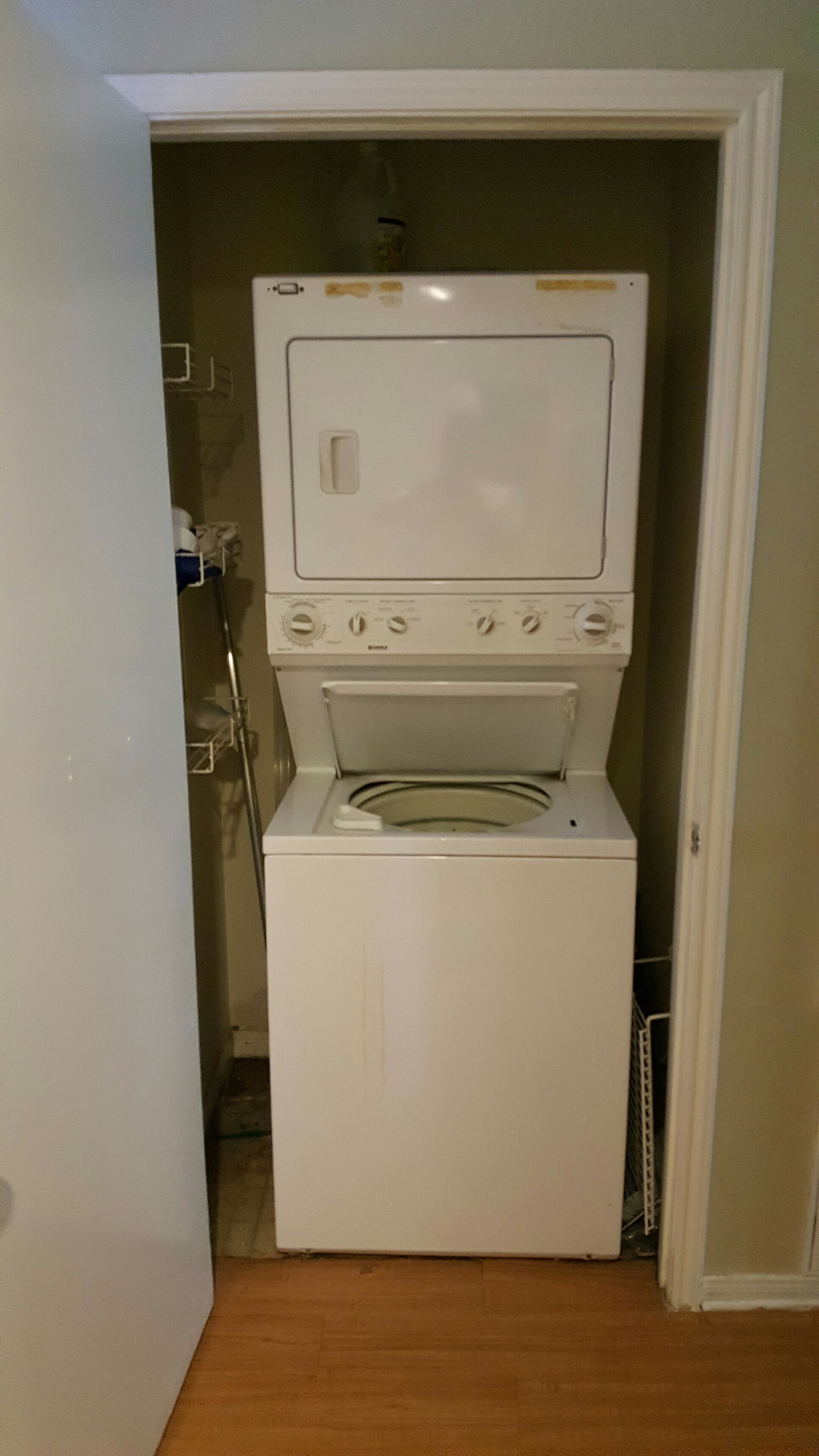 A compact washer and dryer unit in a small laundry room with a wooden floor.