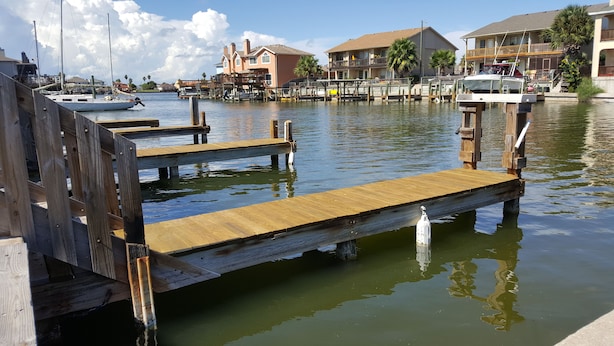A wooden dock extending into calm water with houses in the background. - Perfect ground floor unit ready to entertain your family vacation.  (Corpus Christi)