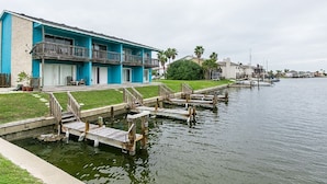 A waterfront hotel with a blue exterior, a grassy deck, and wooden docks leading into the water. - Perfect ground floor unit ready to entertain your family vacation.  (Corpus Christi)