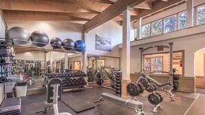 Een sportschool met diverse fitnessapparaten, waaronder gewichten, barbells en fitnessballen.