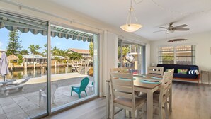 Ein Essbereich mit Tisch und Stühlen, einem Deckenventilator und großen Fenstern mit Blick auf einen Pool und eine Außenlounge.