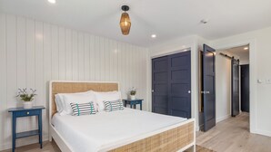Quarto moderno com uma cama grande, duas mesas de cabeceira, uma porta azul escura e um painel de cabeceira trançado.