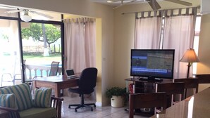 Ein Hotelzimmer mit Essbereich, Fernseher, Schreibtisch mit Laptop, Stuhl, Sofa und Deckenventilator.