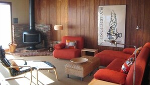 A cozy living room with a fireplace, red sofas, and a wicker ottoman. - Seaside Modern - Easy 3 min Walk to Beach! (Dillon Beach)