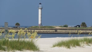 Un faro junto al agua, con una playa arenosa y dunas cubiertas de hierba al frente.