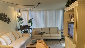 Un salon avec un canapé beige, une table basse en bois et un téléviseur posé sur un meuble.