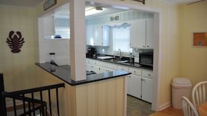A compact kitchen with white cabinets, a black countertop, and a small island. - Steps to the beach.  Pet friendly Beach House w/pool!  4 Bedrooms sleeps 12! (North Myrtle Beach)