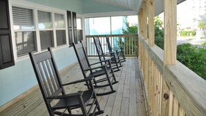 A covered porch with wooden railings and a row of rocking chairs. - Steps to the beach.  Pet friendly Beach House w/pool!  4 Bedrooms sleeps 12! (North Myrtle Beach)